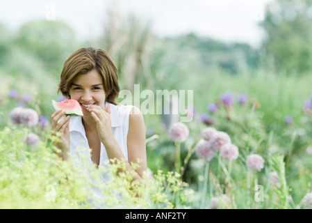 Giovane donna in giardino, mangiando pezzo di anguria Foto Stock