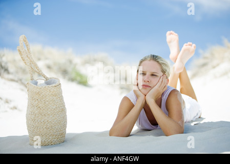 Giovane donna sdraiata sulla spiaggia, borsa da spiaggia nelle vicinanze Foto Stock