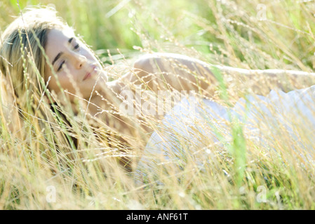 Giovane donna che giace nel campo, rilassante Foto Stock