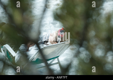 Giovane sciatore di riposo in cattedra sulla neve, rami sfocata in primo piano Foto Stock