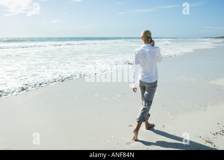 Donna camminare a piedi scalzi sulla spiaggia, tramite telefono cellulare, vista posteriore Foto Stock