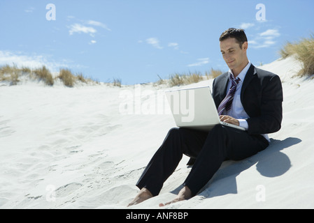 Imprenditore Seduti sulle dune di sabbia, utilizzando laptop Foto Stock