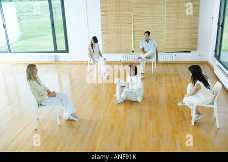 Uomo seduto sul pavimento, tenendo prenota, parlando al gruppo Foto Stock