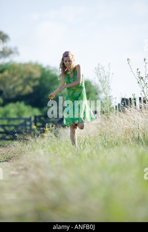 Giovane donna in sundress passeggiando per il settore rurale, fiore di contenimento Foto Stock