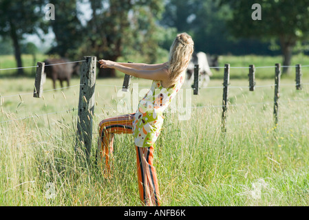 Giovane donna attesa alla recinzione rurale, vista laterale Foto Stock