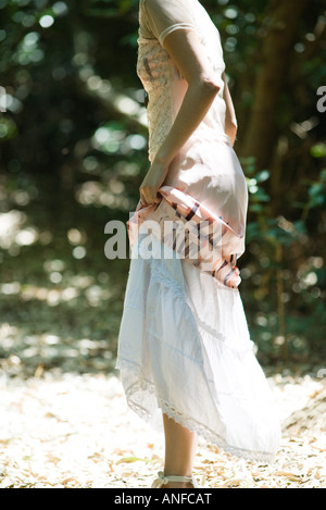 Giovane donna in piedi nei boschi, sollevando la gonna, ritagliato vista laterale Foto Stock