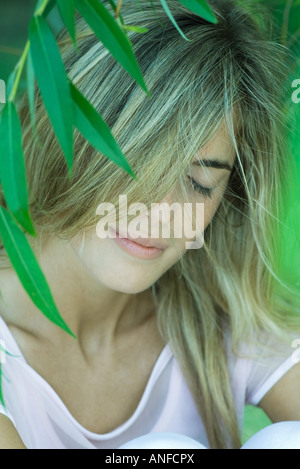 Giovane donna tra le fronde, capelli che ricopre la faccia a occhi chiusi Foto Stock