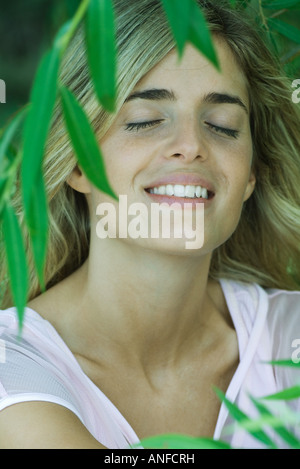 Giovane donna tra le fronde, sorridendo gli occhi chiusi, ritratto Foto Stock