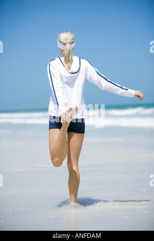 Giovane donna in Active Wear, stiramento sulla spiaggia, vista posteriore Foto Stock