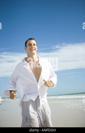Giovane uomo che corre sulla spiaggia, sorridente Foto Stock
