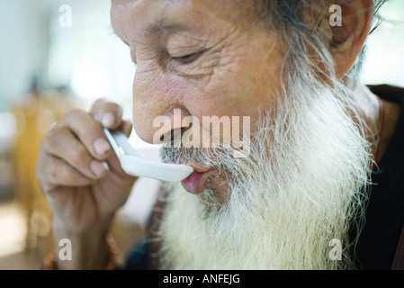 Uomo anziano con la barba lunga di mangiare con cucchiaino cinese Foto Stock