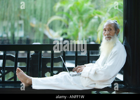 Uomo anziano che indossa il cinese tradizionale abbigliamento, utilizzando laptop a piena lunghezza Foto Stock