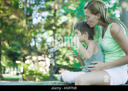 Ragazzo e madre soffiare bolle, vista laterale Foto Stock