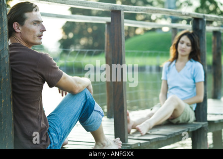 Coppia seduta oltre sul dock, concentrarsi sull'uomo in primo piano Foto Stock