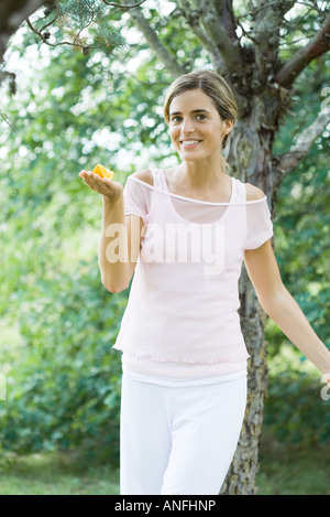 Donna che mantiene fetta d'arancia sul palmo della mano, sorridente in telecamera Foto Stock