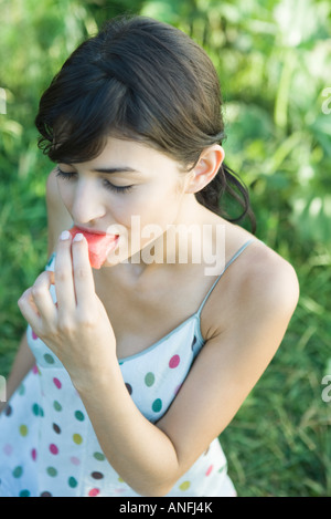 Giovane donna mangiare fetta di frutta, gli occhi chiusi, ad alto angolo di visione Foto Stock