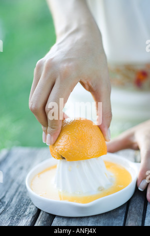 Donna premendo arancione con spremiagrumi, close-up, vista ritagliata delle mani Foto Stock