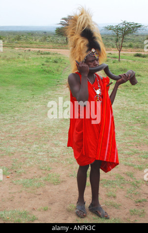 Guerriero Masai e capo del villaggio tribale indossando lion mane copricapo e soffiaggio di corno di antilope durante la cerimonia di benvenuto in Kenya Foto Stock