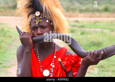 Guerriero masai in Lion Mane headress soffiaggio di corno di antilope Masai Mara village Kenya Africa orientale Foto Stock