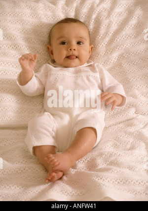 Cheeky baby ragazza distesa su un letto prendendo la sua lingua Foto Stock