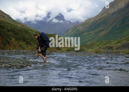 Escursionista attraversa Raven Creek sul Crow Pass Crk Trail AK SC Estate Foto Stock