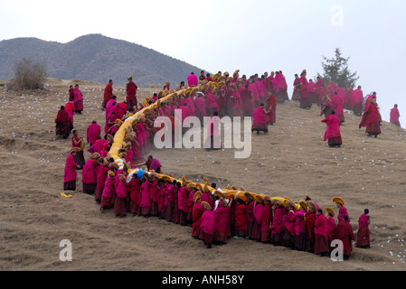 Una lunga fila di monaci carrieng è un enorme Tanka fino a maountain nel monastero di Labrang nella Provincia di Qinghai Cina Foto Stock