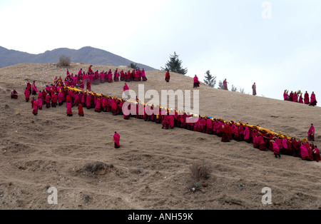 Una lunga fila di monaci carrieng è un enorme Tanka fino a maountain nel monastero di Labrang nella Provincia di Qinghai Cina Foto Stock