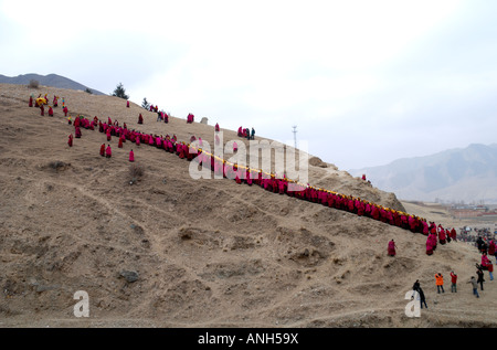 Una lunga fila di monaci carrieng è un enorme Tanka fino a maountain nel monastero di Labrang nella Provincia di Qinghai Cina Foto Stock