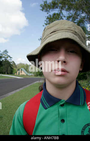 Australian adolescente schoolgirl in uniforme scolastica con il cappello rosso e uno zaino guarda fiducioso e auto garantita Foto Stock