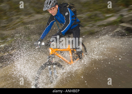 Un mountain biker splash attraverso un fiume in un giorno di pioggia nel distretto del lago, England, Regno Unito Foto Stock