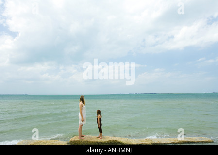 Madre e figlia in piedi dall' oceano, guardando verso l'orizzonte a piena lunghezza Foto Stock