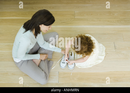 La madre e la bambina seduta sul pavimento, ragazza imparare a legare lacci della scarpa, vista da sopra direttamente Foto Stock