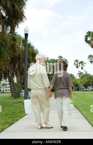 Ragazzo e la nonna camminando sul marciapiede, il trasporto delle borse della spesa, parlare, vista posteriore Foto Stock