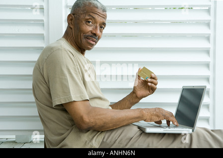 Senior uomo rendendo carta di credito acquisto on line, sorridente in telecamera Foto Stock