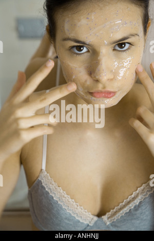 Giovane donna di applicare la maschera per il viso, guardando la telecamera, close-up Foto Stock