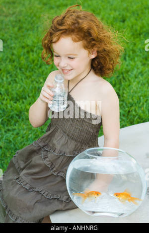 Ragazza seduta accanto a Goldfish Bowl, acqua potabile Foto Stock