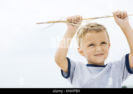 Ragazzo giovane azienda fino in stick, bracci sollevati, sorridente Foto Stock