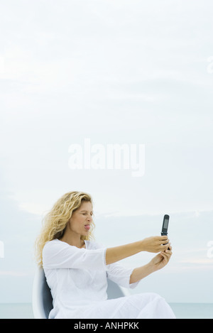 Donna fotografare auto con un telefono cellulare, spuntavano lingua a occhi chiusi Foto Stock