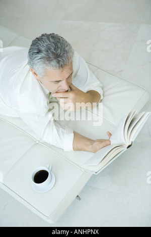 Coppia uomo disteso sulla chaise longue con la mano sotto il mento, la lettura di libri, ad alto angolo di visione Foto Stock