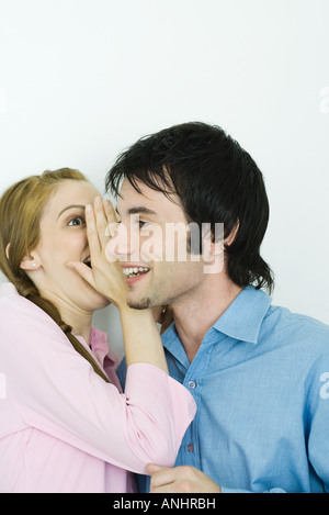 Giovane donna whispering nell uomo l orecchio, close-up Foto Stock