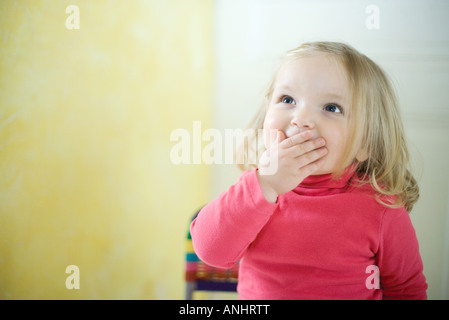 Bionda ragazza toddler che copre la bocca, cercando Foto Stock