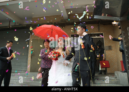 Nozze cinesi, la sposa e lo sposo lasciando sotto i confetti, sposa coperti da Ombrellone rosso Foto Stock