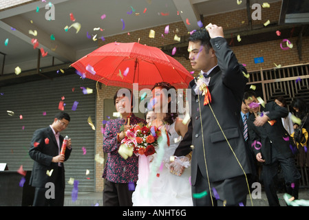 Nozze cinesi, la sposa e lo sposo lasciando sotto i confetti, sposa coperti da Ombrellone rosso Foto Stock