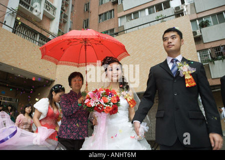 Nozze cinesi, la sposa e lo sposo lasciando sotto i confetti, sposa coperti da Ombrellone rosso Foto Stock