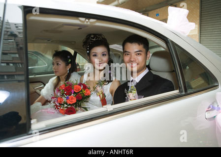 Sposa e lo sposo in auto con damigella, sorridente in telecamera Foto Stock