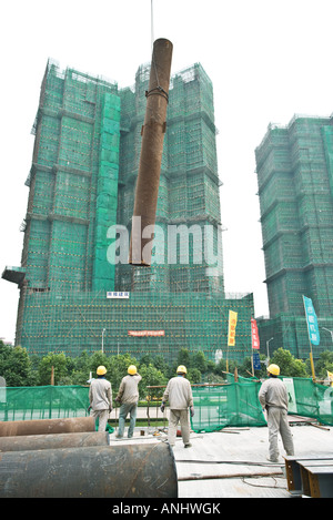 Operai della costruzione al cantiere, il tubo essendo sollevato in aria Foto Stock