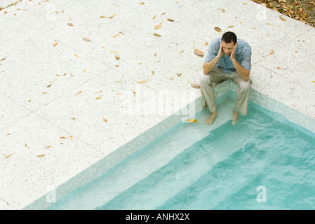 Uomo seduto con i piedi in piscina, tenendo testa, ad alto angolo di visione Foto Stock