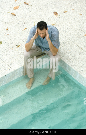 Uomo seduto con i piedi in piscina, tenendo testa, ad alto angolo di visione Foto Stock