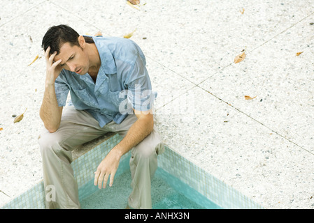 Uomo seduto con i piedi in piscina, tenendo testa, ad alto angolo di visione Foto Stock