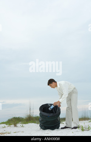 Uomo in spiaggia, immissione di acqua in bottiglia in immondizia può Foto Stock